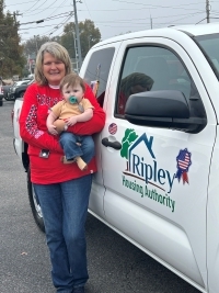 A lady holding a baby next to a white Ripley Truck.